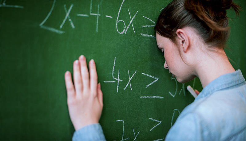 Teenager girl in math class overwhelmed by the math formula. Pressure, Education, Success concept. Student with head against blackboard.