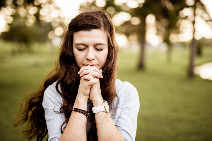 Closeup shot of a female with her hands near the mouth while praying with a blurred background