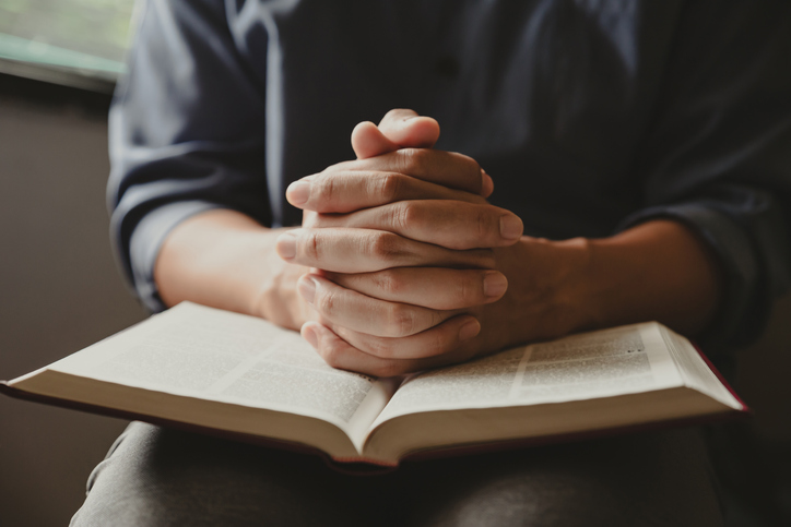 Hands of man praying to god with the bible.