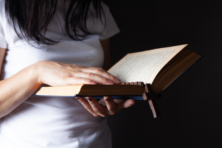 woman praying holding book and cross