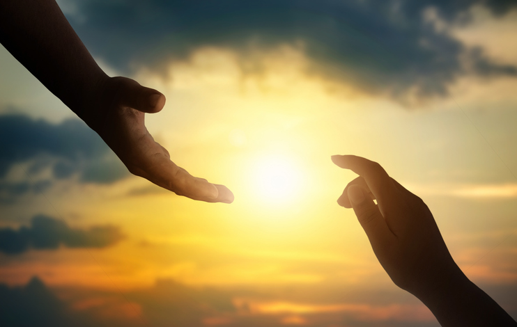 Silhouettes of hands reaching out for hope and supporting each other on sunset background.