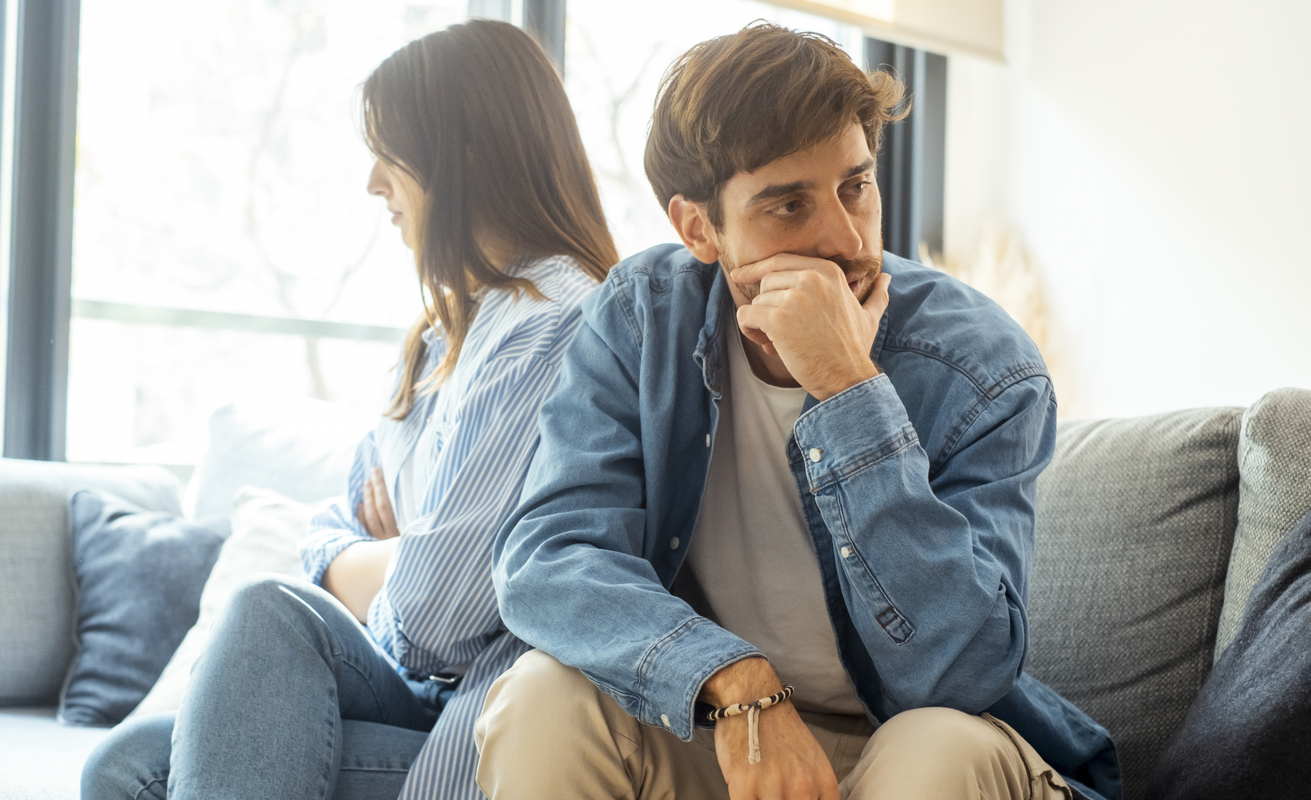 Engaged couple with relationship problems sitting on the sofa with their backs to each other after an argument, conflicts in marriage, upset couple after a dispute, making decision to break up and divorce