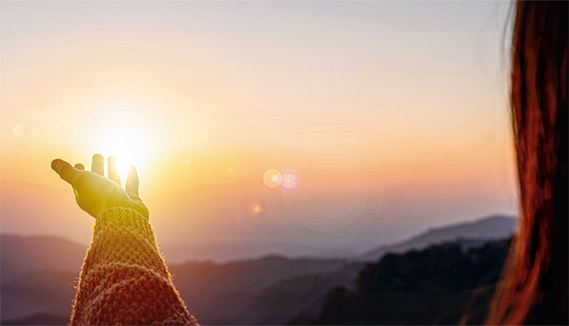 Young woman hand reaching for the mountains during sunset and beautiful landscape