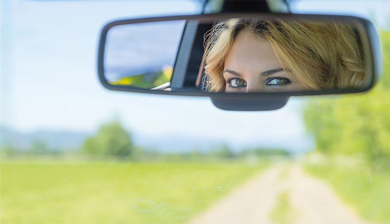 The beautiful eyes of the young driver woman are reflected in the rearview mirror