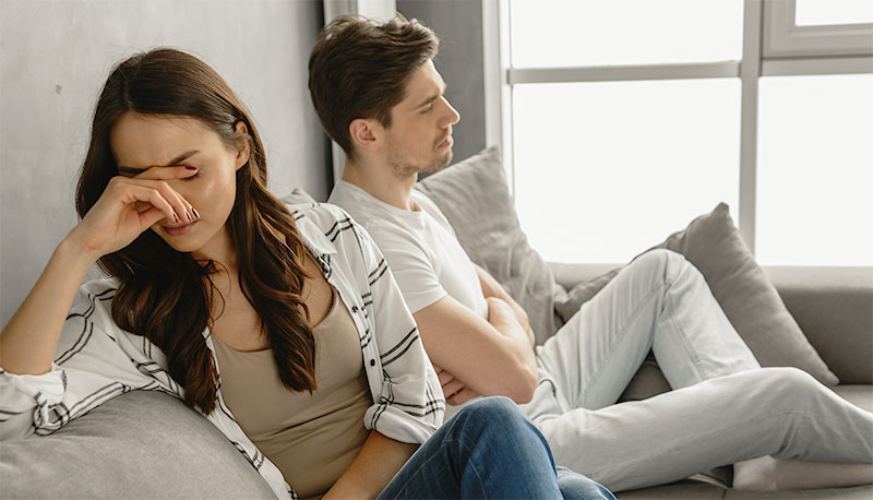 Photo of disappointed couple sitting together on sofa at home with upset look and expressing quarrel, isolated over white background