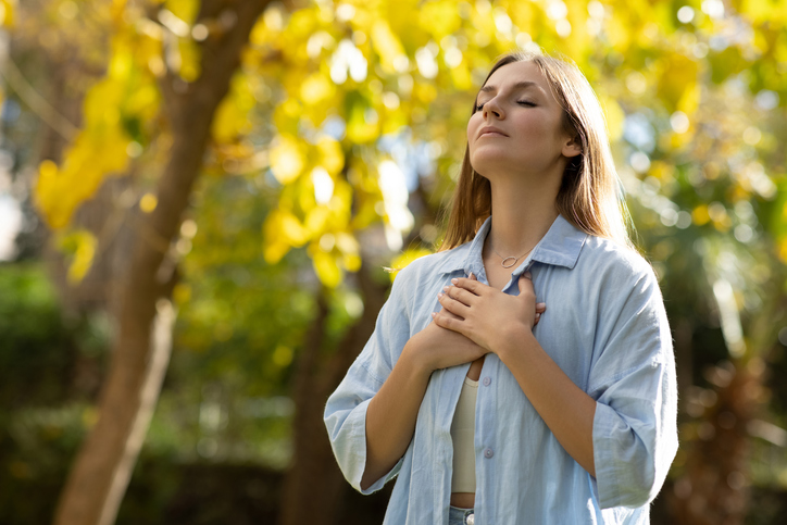 Woman with closed eyes putting hands on her chest