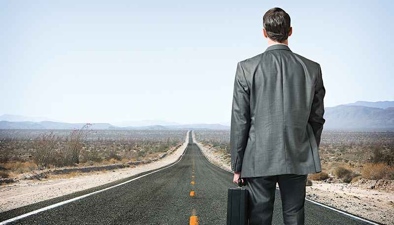 Businessman holding briefcase looking down long desert highway