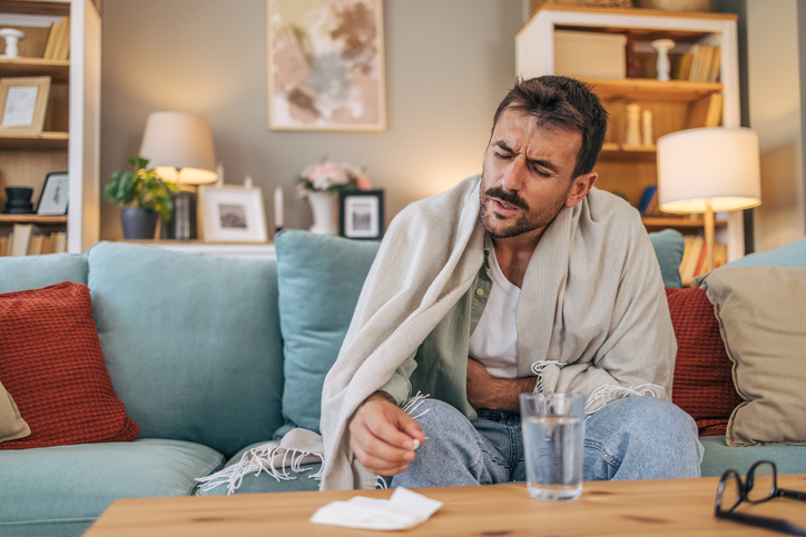 A sick mid adult man is sitting on a sofa.