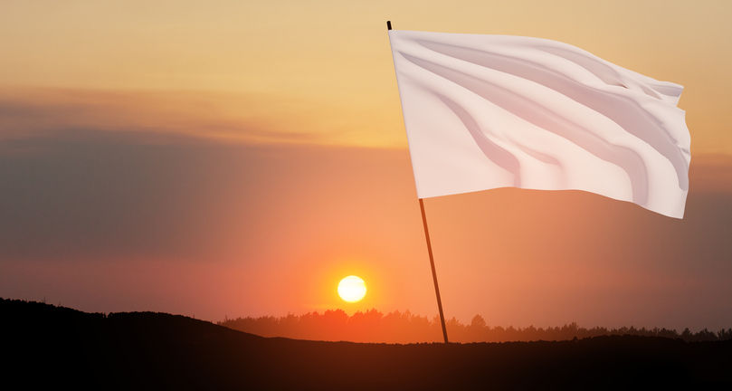 White flag waving in the wind on flagpole against the sunset sky with clouds.