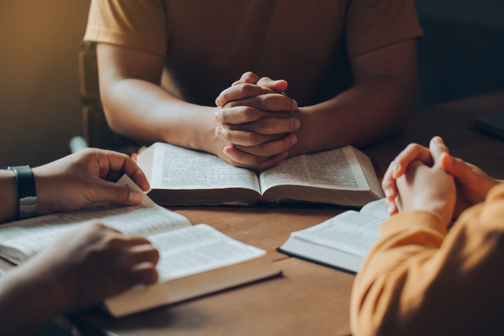 Christians and Bible study concept.Christian family sitting around a wooden table with open bible page and holding each other&#8217;s hand praying together.