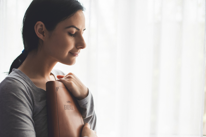 Portrait of a woman with a surgical mask on her face and a bible held tight to her chest