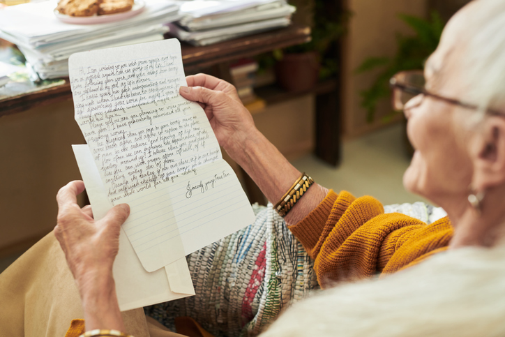 Elderly Person Reading Handwritten Letter by Desk