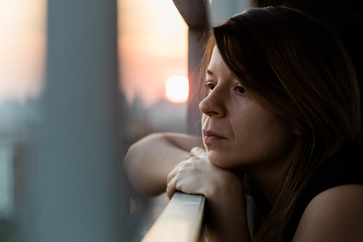 Young sad woman looking outside through balcony of an apartment building