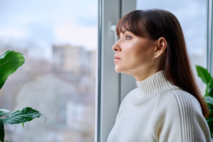 Serious thoughtful middle aged female looking out the window at home