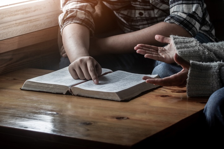 Two young christianity sitting around wooden table with open holy bible and praying to God together.