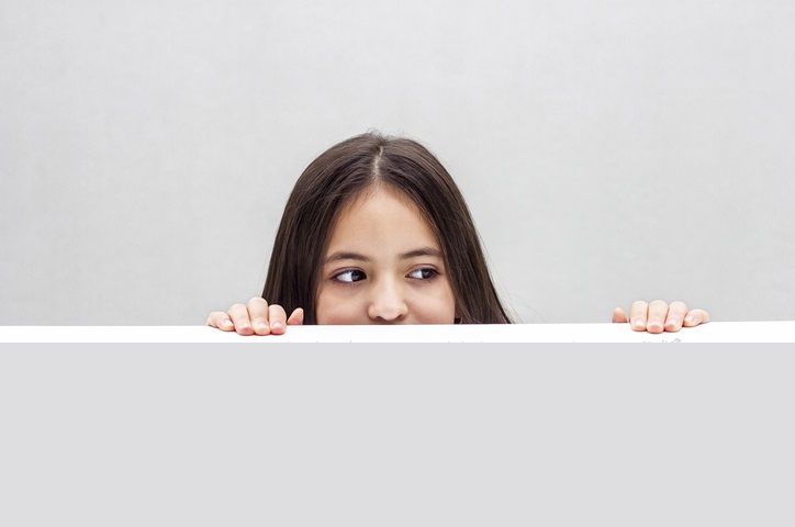 Girl looks out from behind the table. isolated on white background