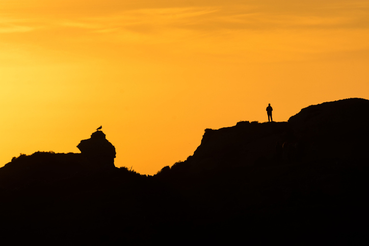 people stand on top of the mountain in silhouette as the sun sets