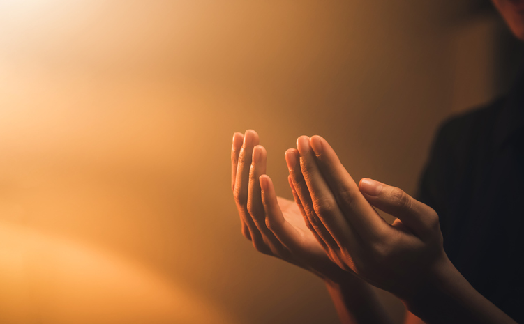 Hand praying on orange light bokeh background.