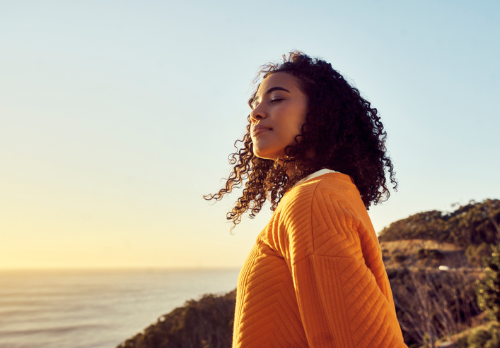Freedom, relax and happy mindset of a woman from Brazil with sun on her face at a sea. Nature, ocean and beach water sunset with a young person feeling peace, wellness and gratitude from meditation