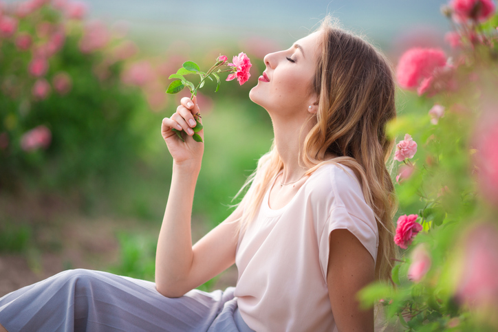 Beautiful young girl is wearing casual clothes having rest in a garden with pink blossom roses