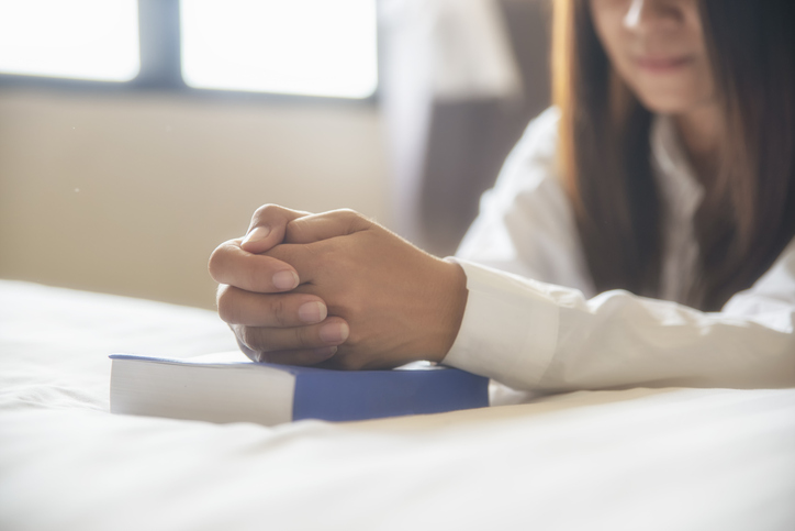 Pray and bible concept, Beautiful woman (christian) praying by hand in hand together on bible, thinking and closed her eyes. Person side view, Asian female hope for peace and read bible at bedroom.