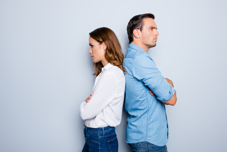 Portrait of unhappy frustrated couple standing back to back not speaking to each other after an argument while standing on grey background. Negative emotion face expression reaction