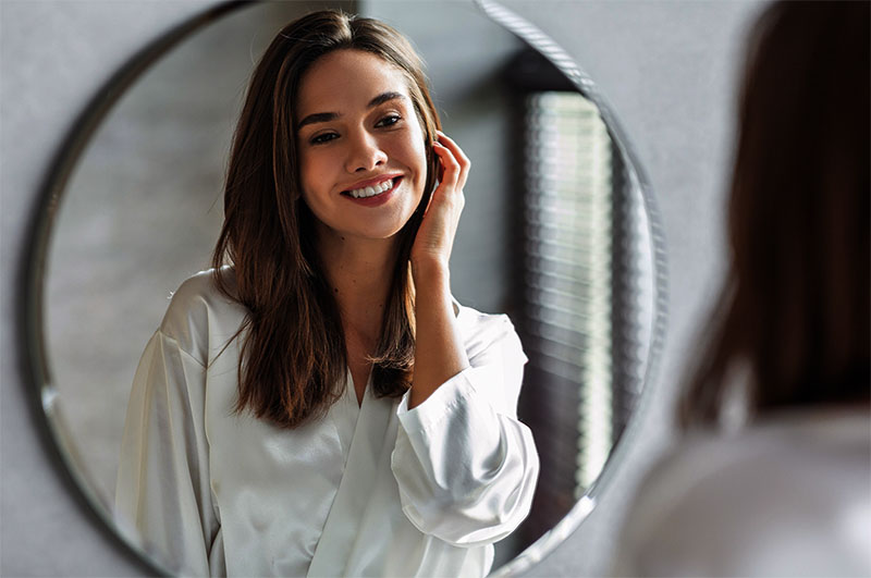 Beauty Concept. Portrait Of Attractive Happy Woman Looking At Mirror In Bathroom