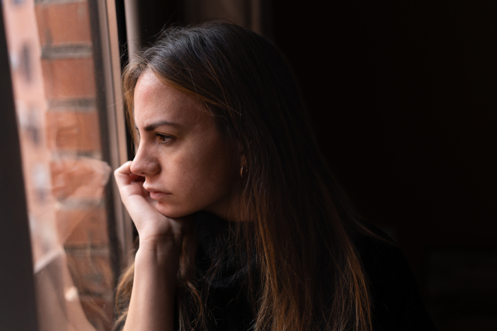 Upset woman looking out window at home