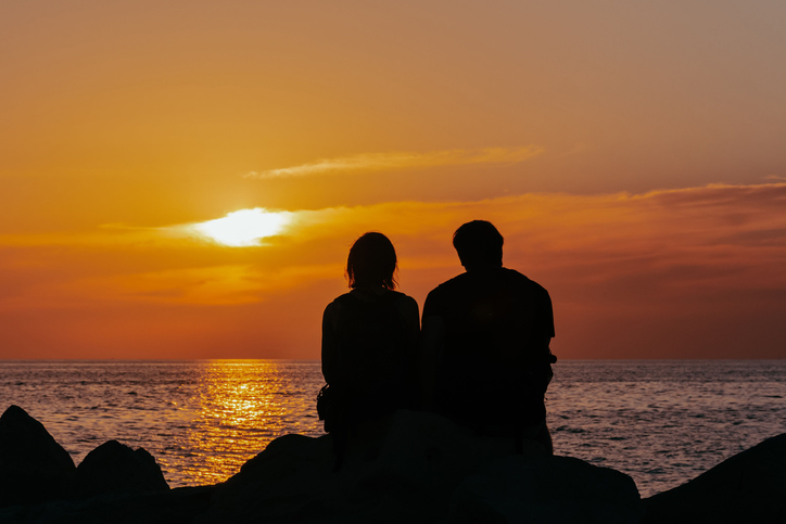 Silhouettes of a couple enjoying sunset over the ocean sitting on the rock