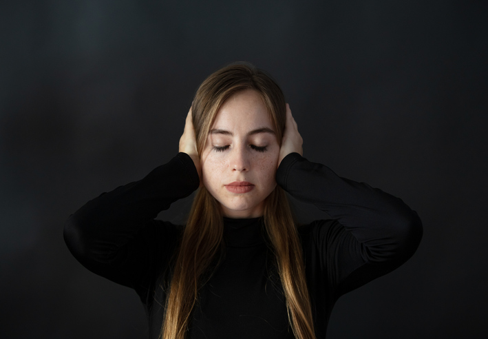 Blond woman with closed eyes covering her ears with her hands.