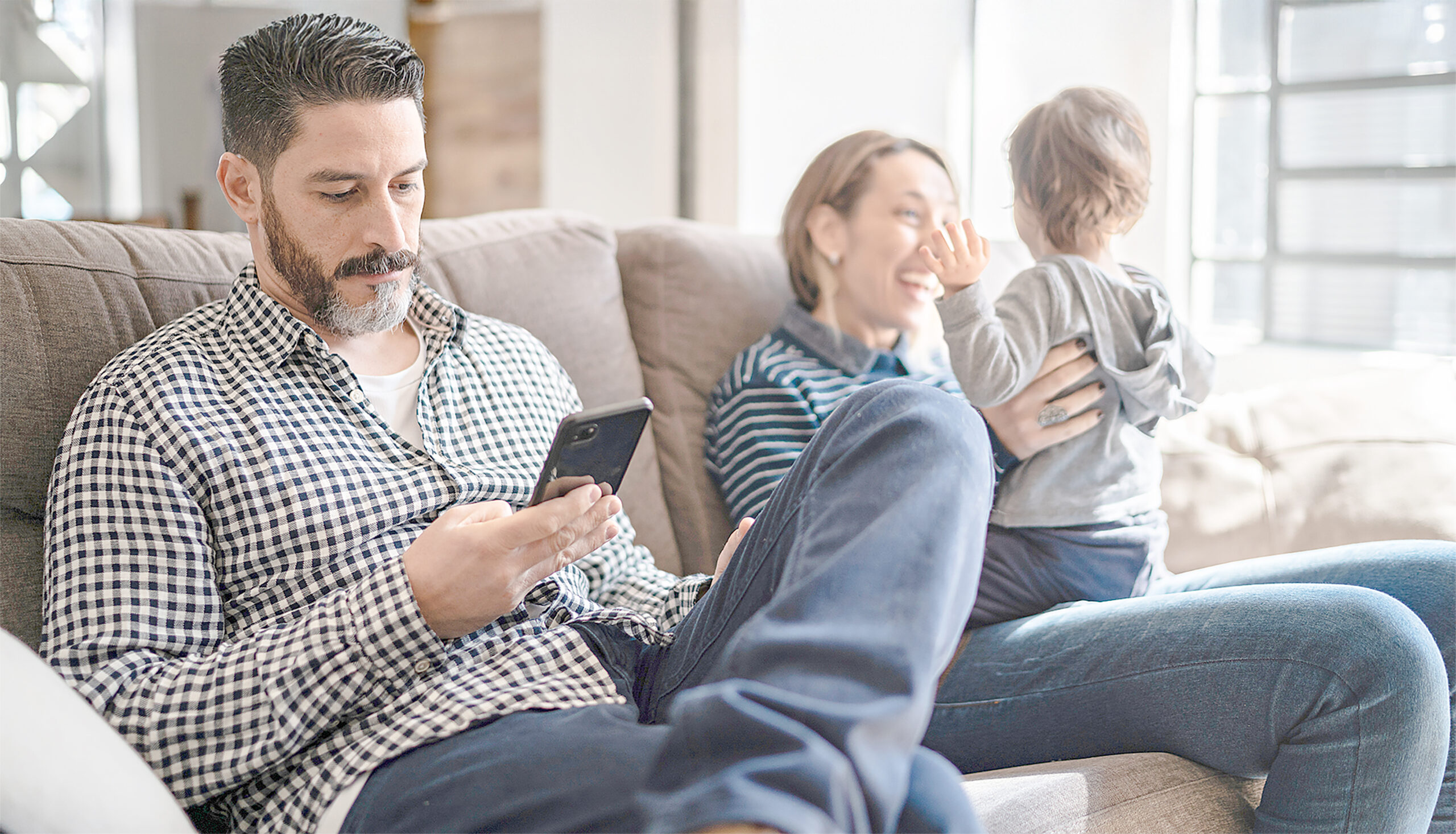 Man using smartphone and mother playing with son