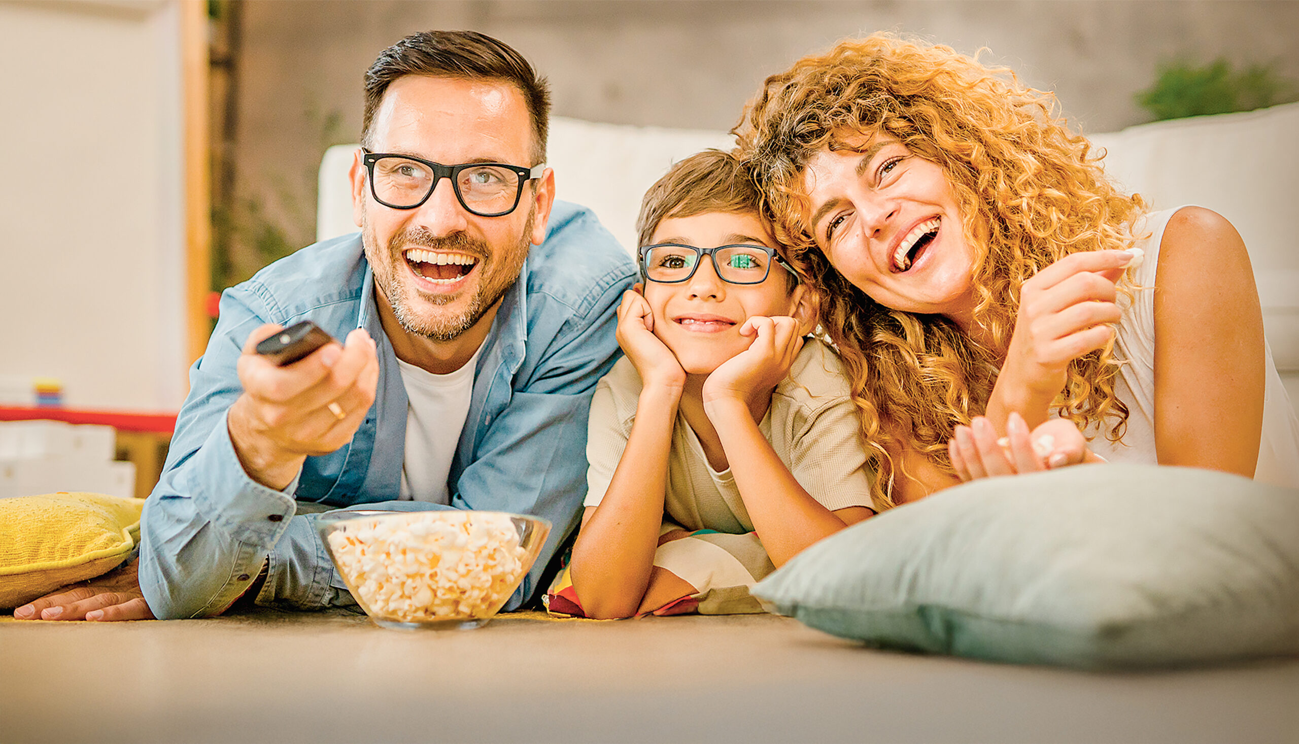 Family -father, mother and son enjoying at home sitting on the floor eating popcorns while watching TV