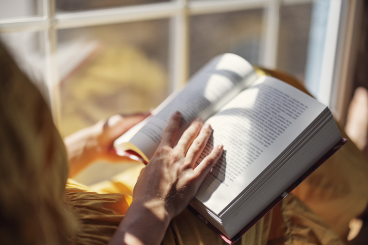 Teenage girl sitting on windowsill and reading a book
