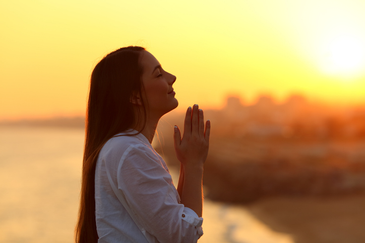 Profile of a woman praying at sunset