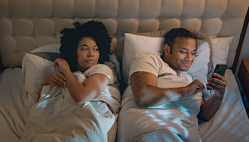 African American couple family in bed bedroom at night angry frustrated woman wife trying sleep offended on husband man gadget addict chatting with phone laughing mobile smartphone addiction problem