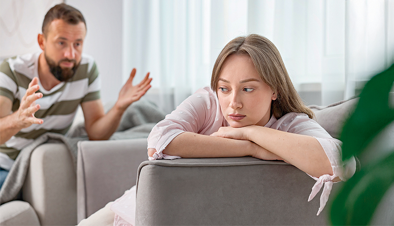 Betrayal. Man talking to his offended wife on sofa at home, selective focus