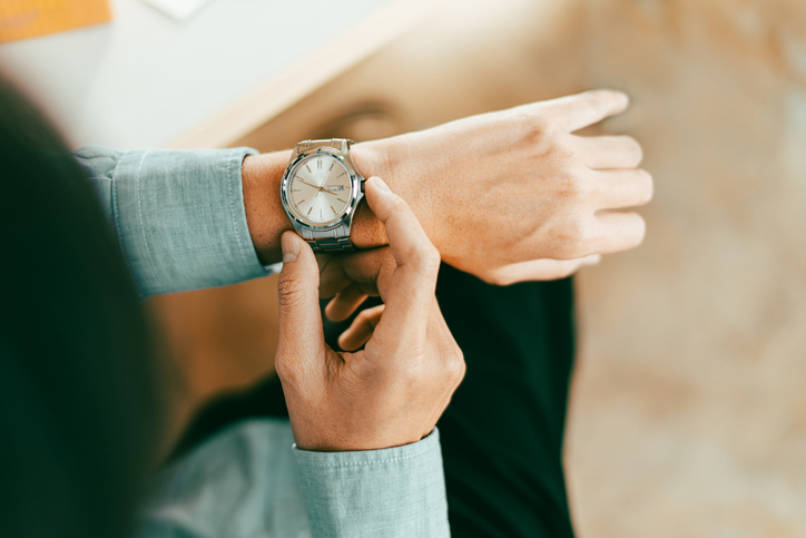 businessman in casual fashion checks his stainless wristwatch is waiting for his next appointment focused on time cooperation and consulting, topview above.