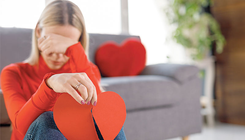 Sad young woman holding a broken heart made out of paper and crying