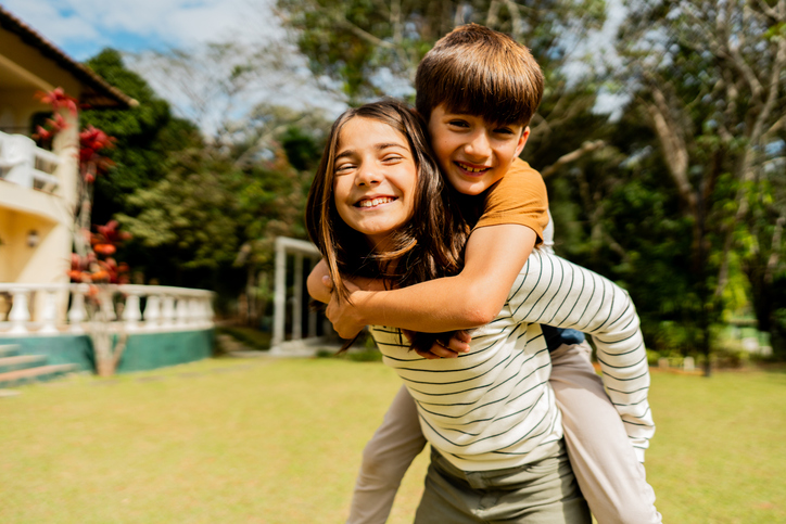 Portrait of a sister piggybacking her brother in the backyard at home