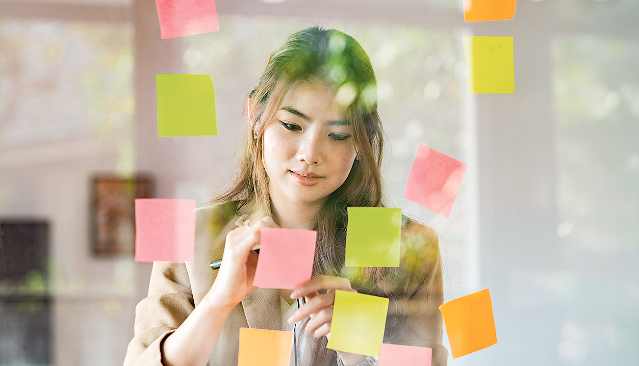 Asian businesswomen use post-it notes on glass walls to write strategy business plans to development grow to success