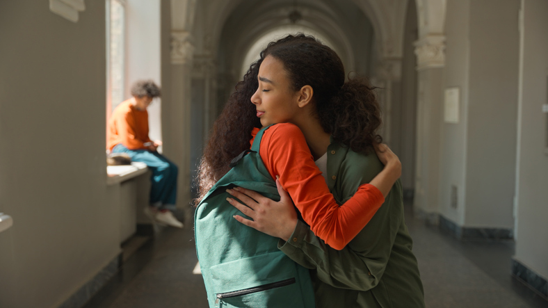 Hispanic sad upset frustrated woman student walking in college university corridor hall girl female friend meeting talking supporting calming girls students hugging friendship help care problem school